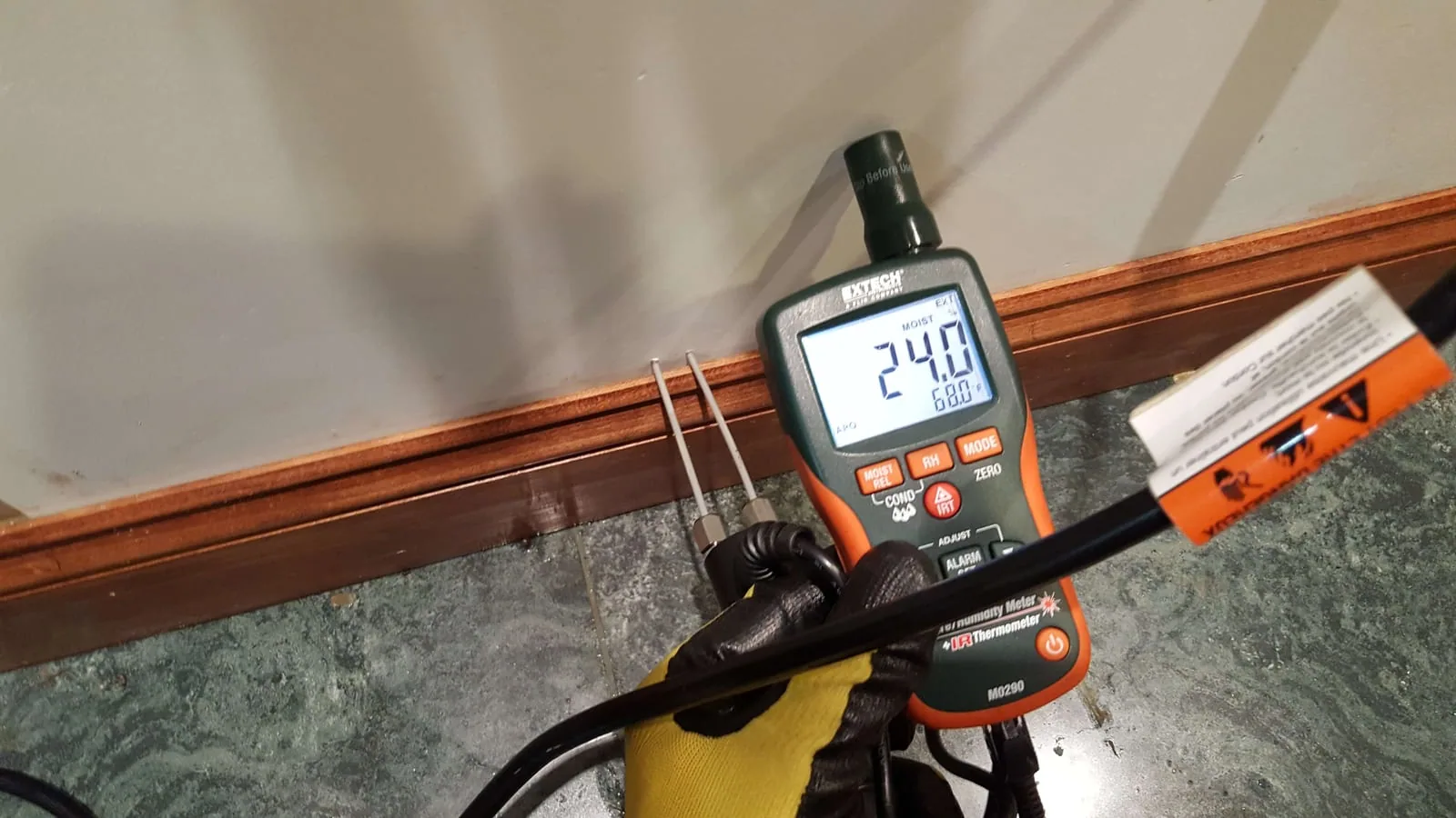Extech pin-type moisture meter showing 24% reading at a wet baseboard during water damage inspection