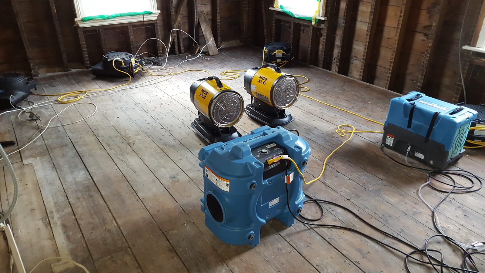 Industrial air movers, heaters, and a dehumidifier drying a gutted room down to the studs