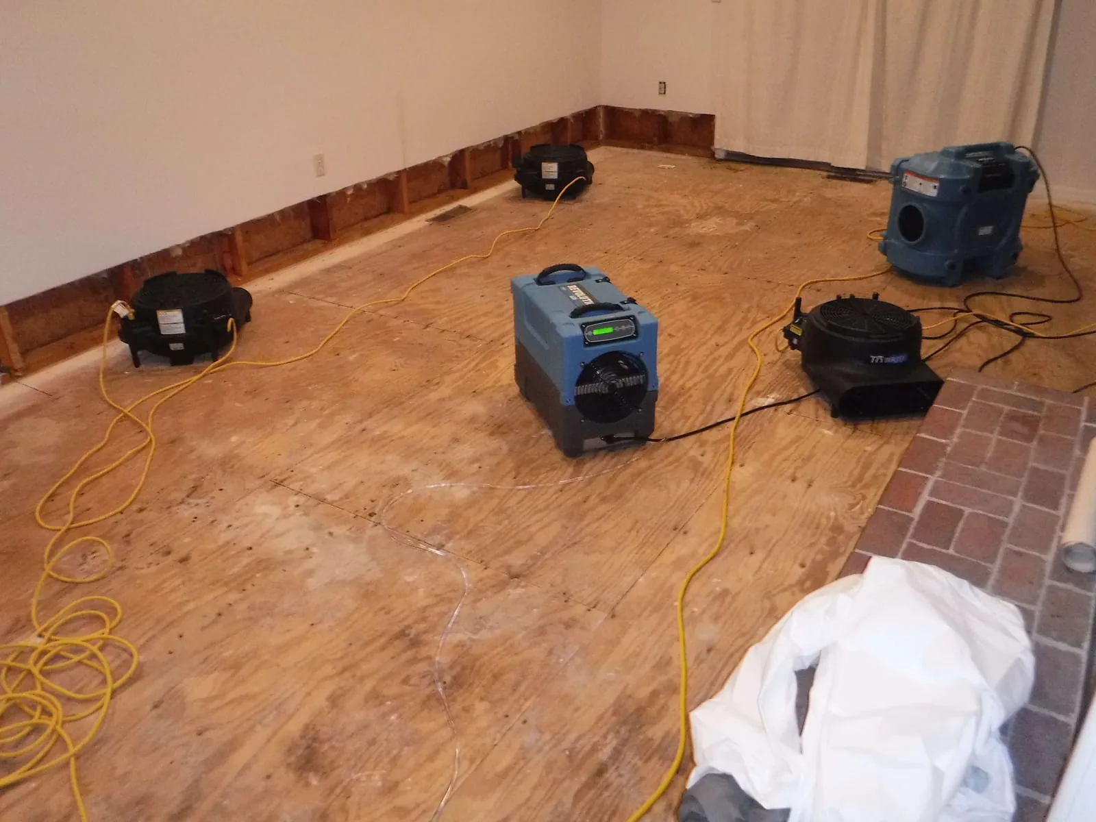 Multi-unit structural drying setup with LGR dehumidifiers and air movers on plywood subfloor